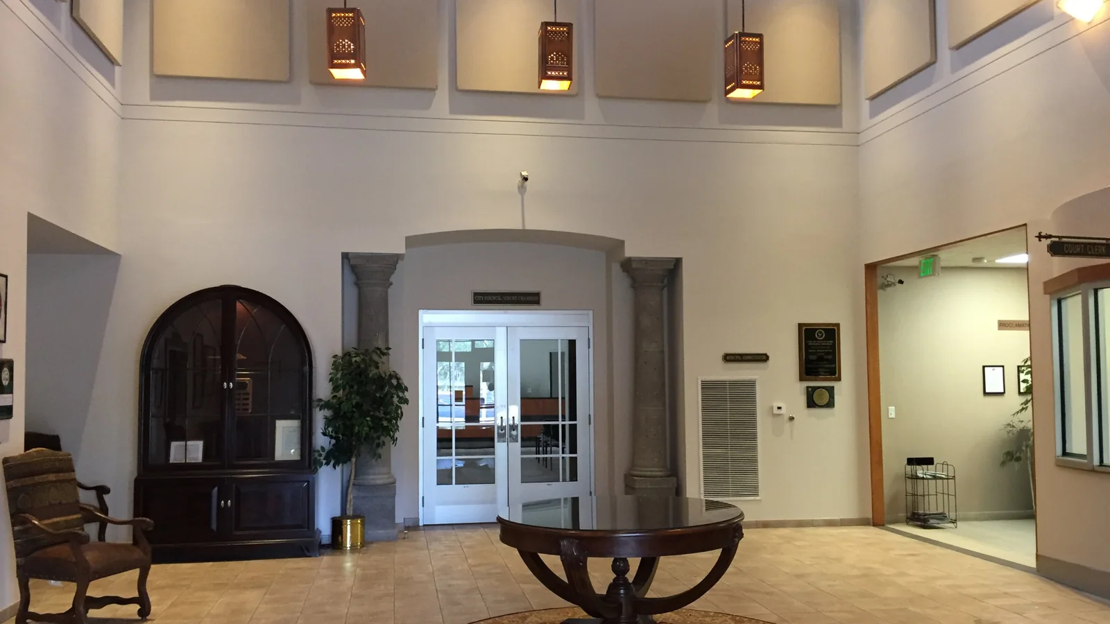 Double height lobby with pendant lantern fixtures, large smooth painted walls and an arched entry framed by stone columns