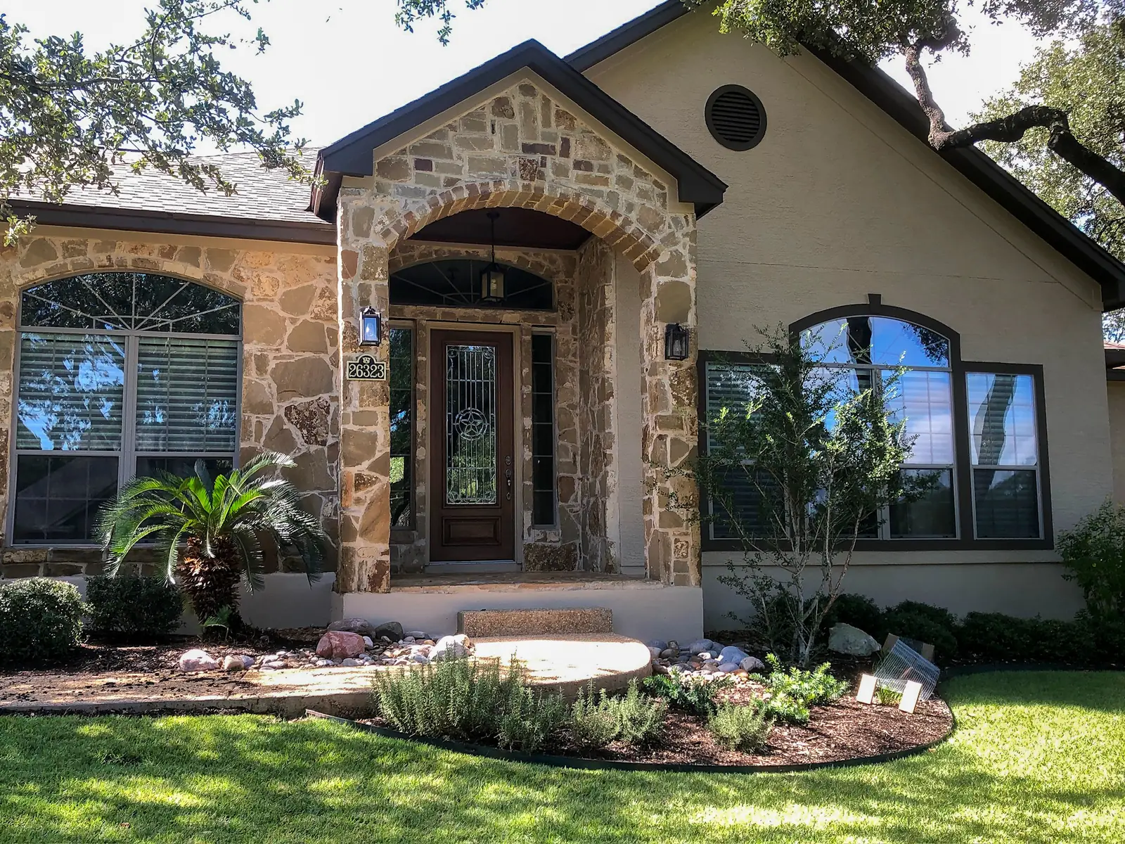 Single story stucco home with a limestone arched entry, a dark wood front door, arched windows and landscaped beds
