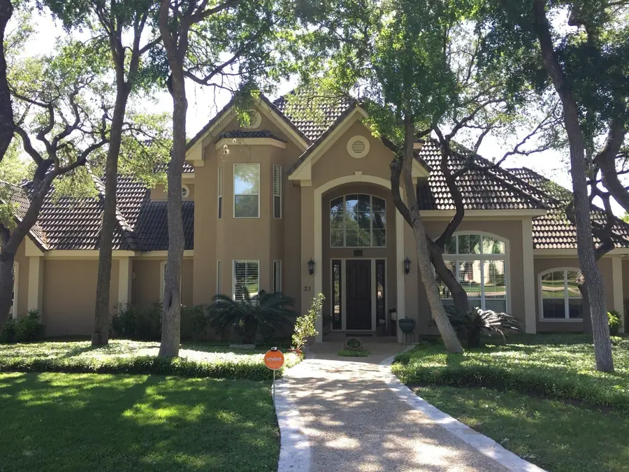 Two story stucco home with a tile roof under mature live oaks, long front walk in dappled light