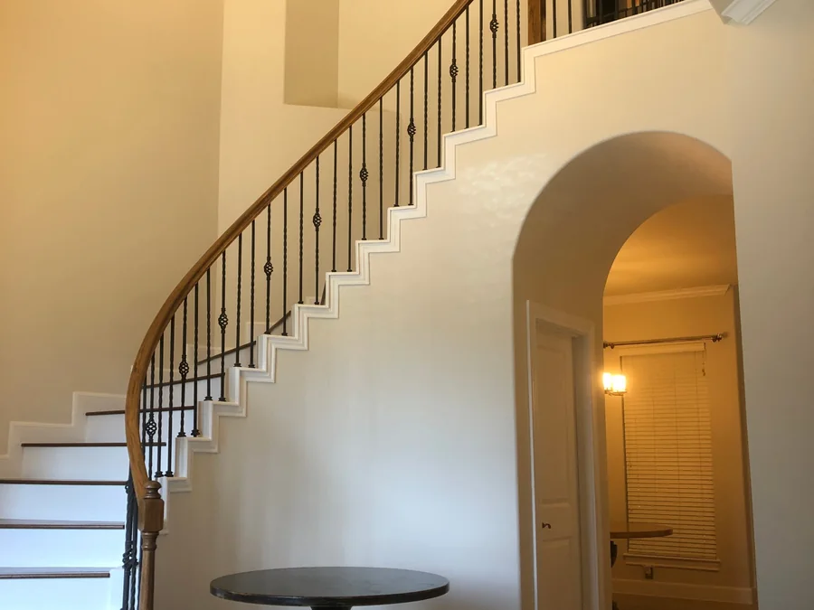 Two story entry with a curved staircase, iron balusters, white risers and trim beside an arched opening, repainted by Value House Painting