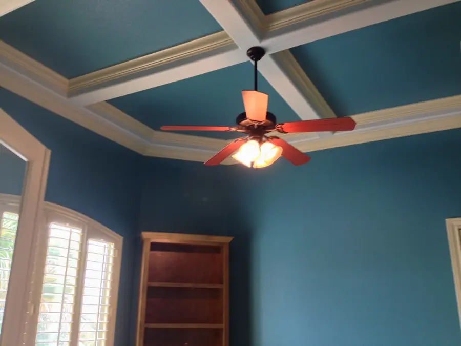 Teal coffered ceiling with white beams, a dark ceiling fan and plantation shutters after repainting